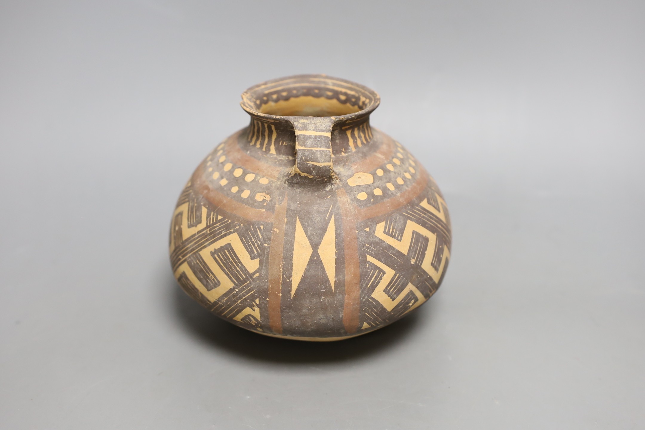 A Chinese pigment painted pottery two handled jar, possibly Neolithic, 14cm high